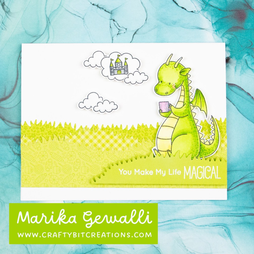 Handmade card with grass on bottom made from multiple layer of pattern paper with a dragon sitting on top and thinking about a castle and a sentiment you make my life magical