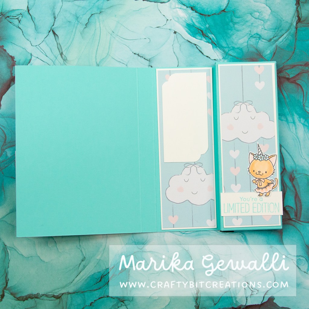 Close up images of the inside of a blue-green box card covered in pattern paper with clouds and strings of hearts. The opened card has a sentiment in the lower right corner saying "you are a limited edition", on top of the sentiment is a unicorn cat with a skirt and a bow.