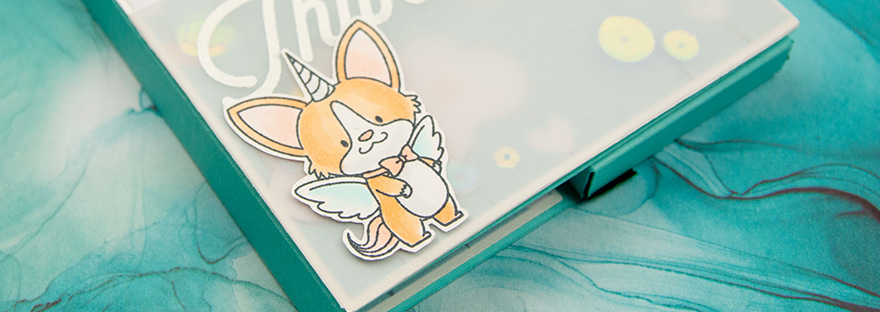 Feature image of close up of the lower left of a blue-green box card depicting a winged unicorn corgi. Image used to give a teaser of post.