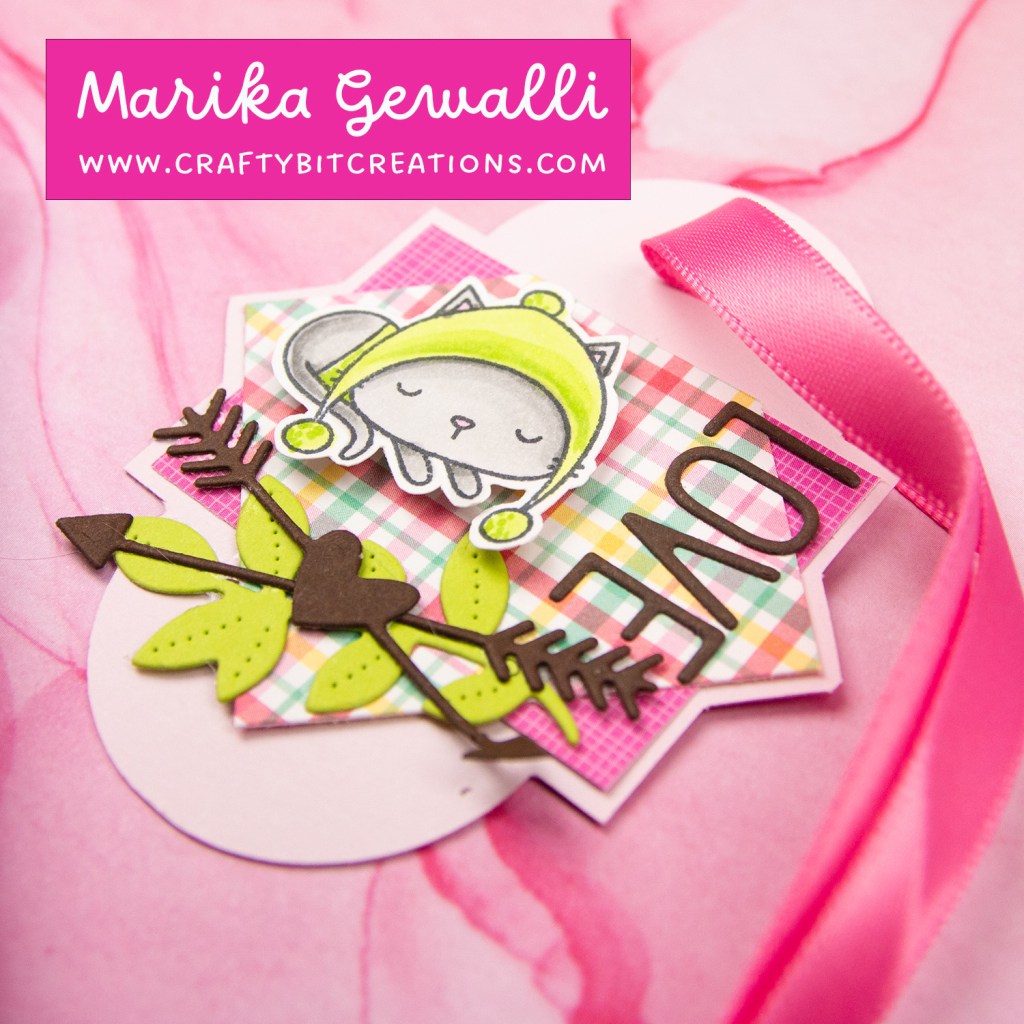 close up of light pink tag, pattern paper and diecut branch and arrows layered with the text love and a stamped and colored cat