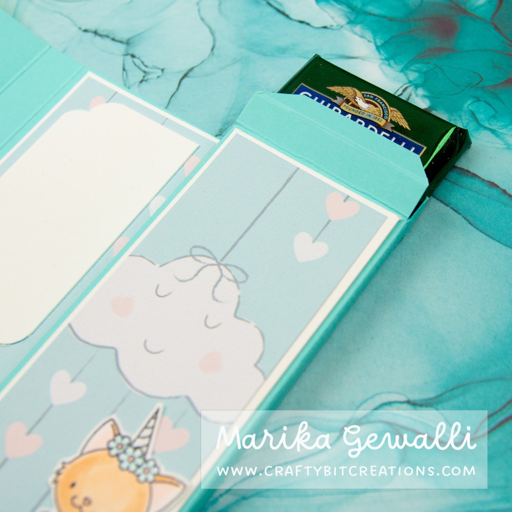 Close up images of the inside of a blue-green box card covered in pattern paper with clouds and strings of hearts. The box is open and a ghiraddelli chocolate square sticks out.