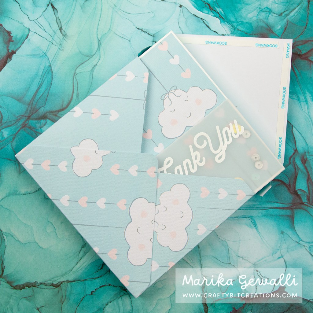 Close up images of a blue-green box card covered in pattern paper with clouds and strings of hearts. The card sticks out of an envelope.